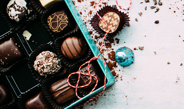 A hand delivering a beautifully wrapped box of chocolates on a cobblestone street.