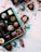 An assortment of decorative chocolate pieces placed in a blue box, with colorful wrapping scattered around. Red strings and ribbons are artistically strewn across a white surface dusted with cocoa powder.