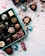 An assortment of decorative chocolate pieces placed in a blue box, with colorful wrapping scattered around. Red strings and ribbons are artistically strewn across a white surface dusted with cocoa powder.