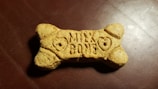 A dog biscuit shaped like a bone with the words 'Milk Bone' engraved on its surface, placed on a textured, dark brown background.