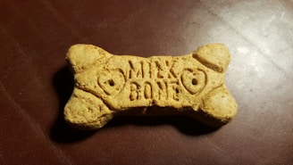 A dog biscuit shaped like a bone with the words 'Milk Bone' engraved on its surface, placed on a textured, dark brown background.