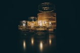 A group of glass jars with lit candles inside, wrapped with striped decorative bands, creating a warm and serene atmosphere.