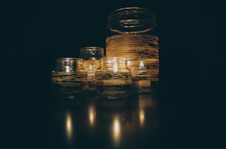 A group of glass jars with lit candles inside, wrapped with striped decorative bands, creating a warm and serene atmosphere.