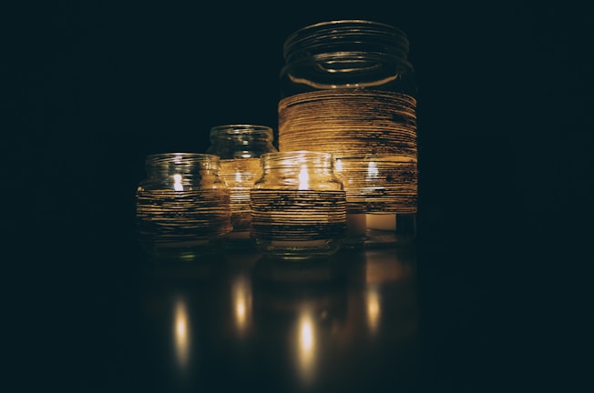 A group of glass jars with lit candles inside, wrapped with striped decorative bands, creating a warm and serene atmosphere.