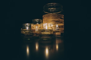 A group of glass jars with lit candles inside, wrapped with striped decorative bands, creating a warm and serene atmosphere.