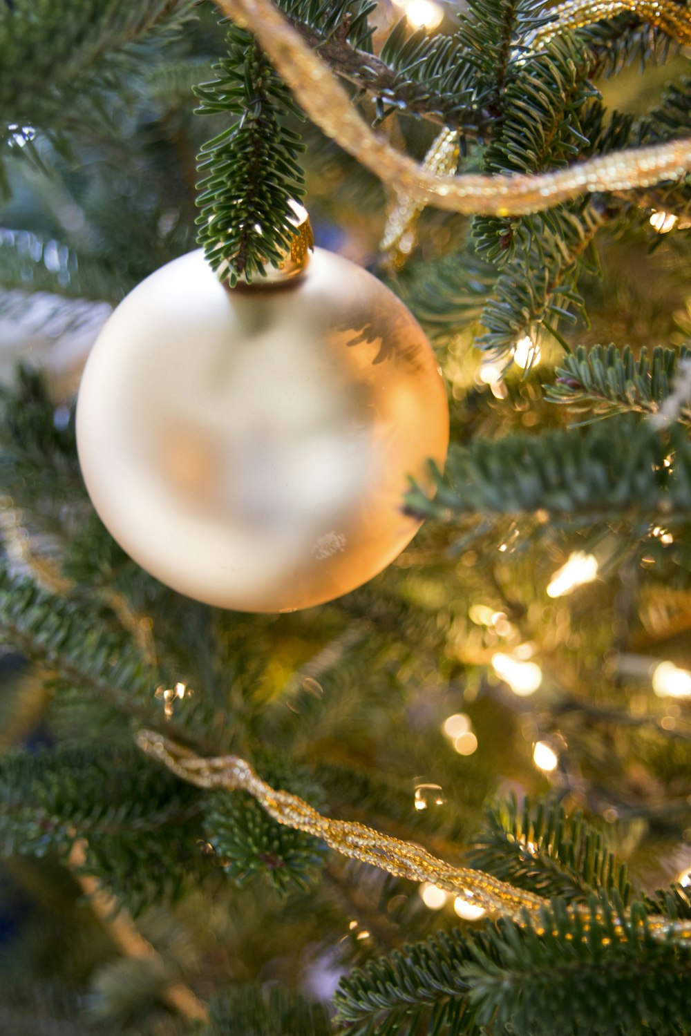 A white Christmas ornament hanging from a lit XMAS tree.