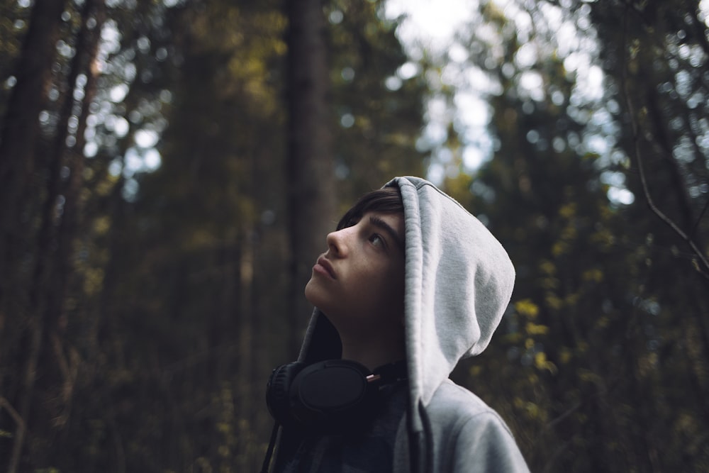 Person wearing a hoodie and headphones looks up in the woods