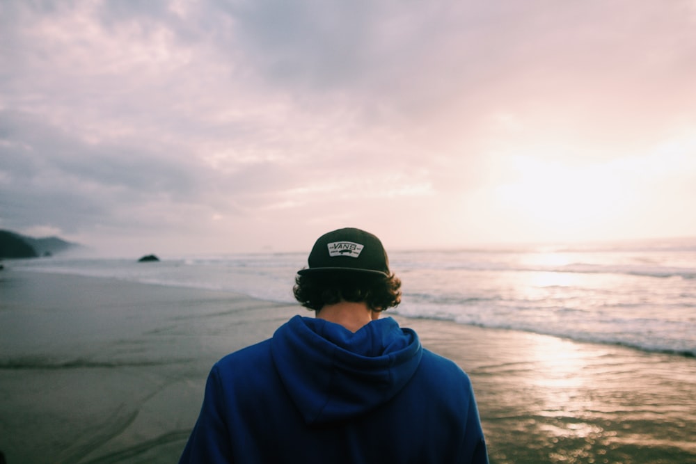 man wearing fitted cap standing on shore at dusk