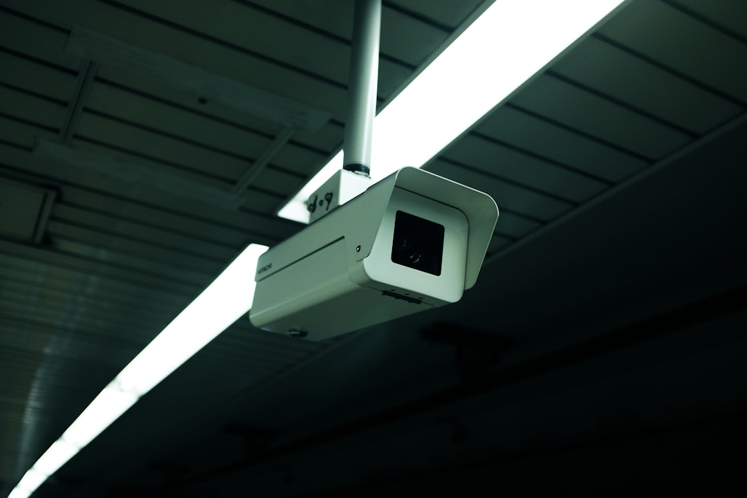 White surveillance camera monitoring a dark space with lined ceilings and overhead lights