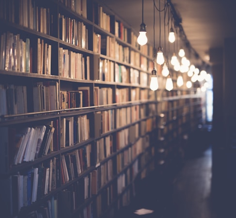 Person sitting with stack of books looking contemplative by window