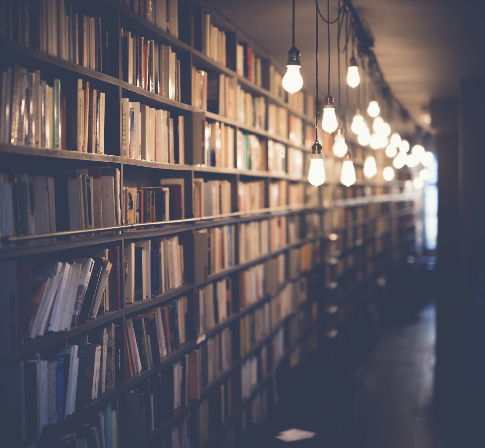 Library shelves with books and hanging pendant lights illuminating the corridor
