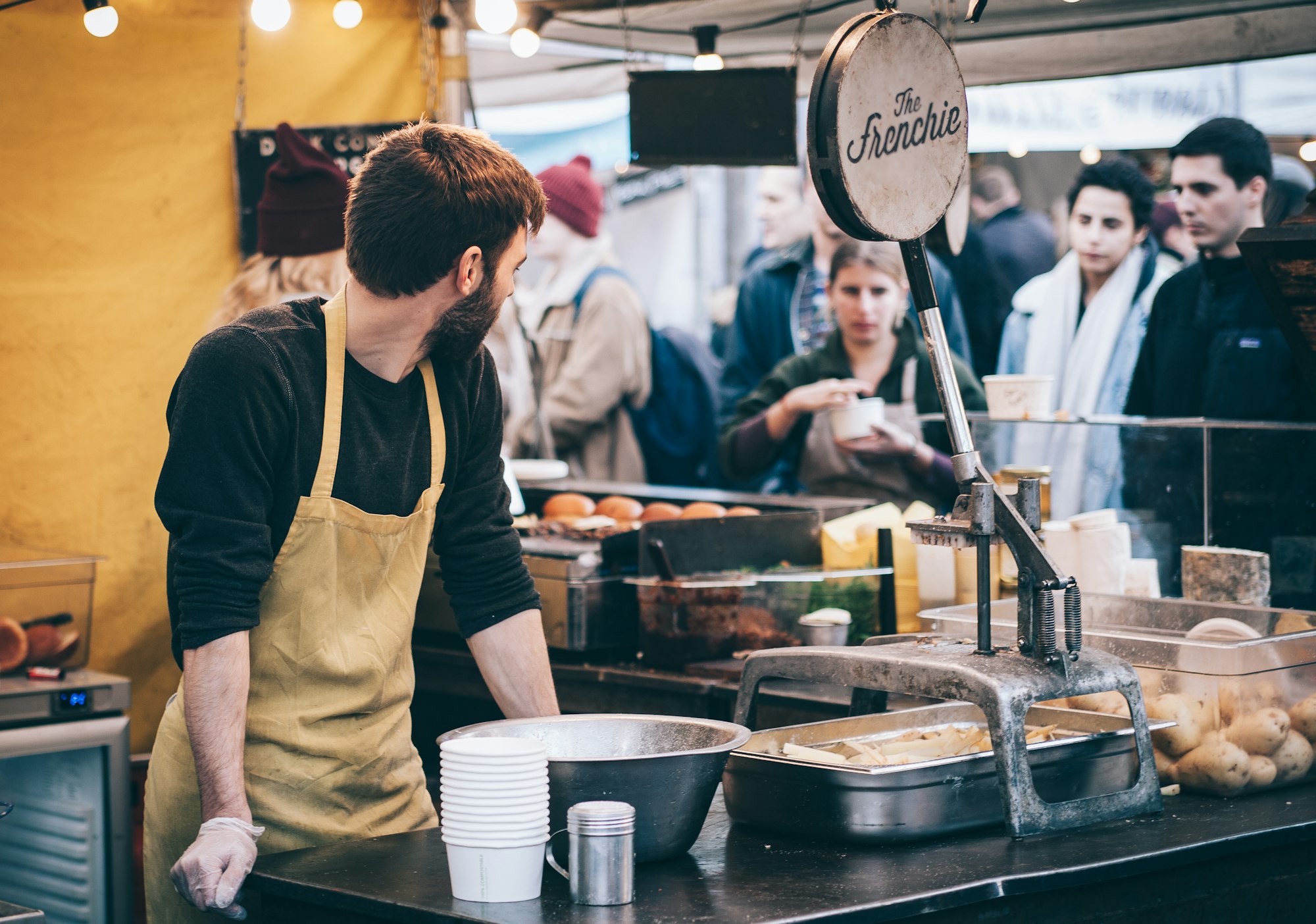 Restaurant staff worker in kitchen in front of food items as restaurant guests watch.