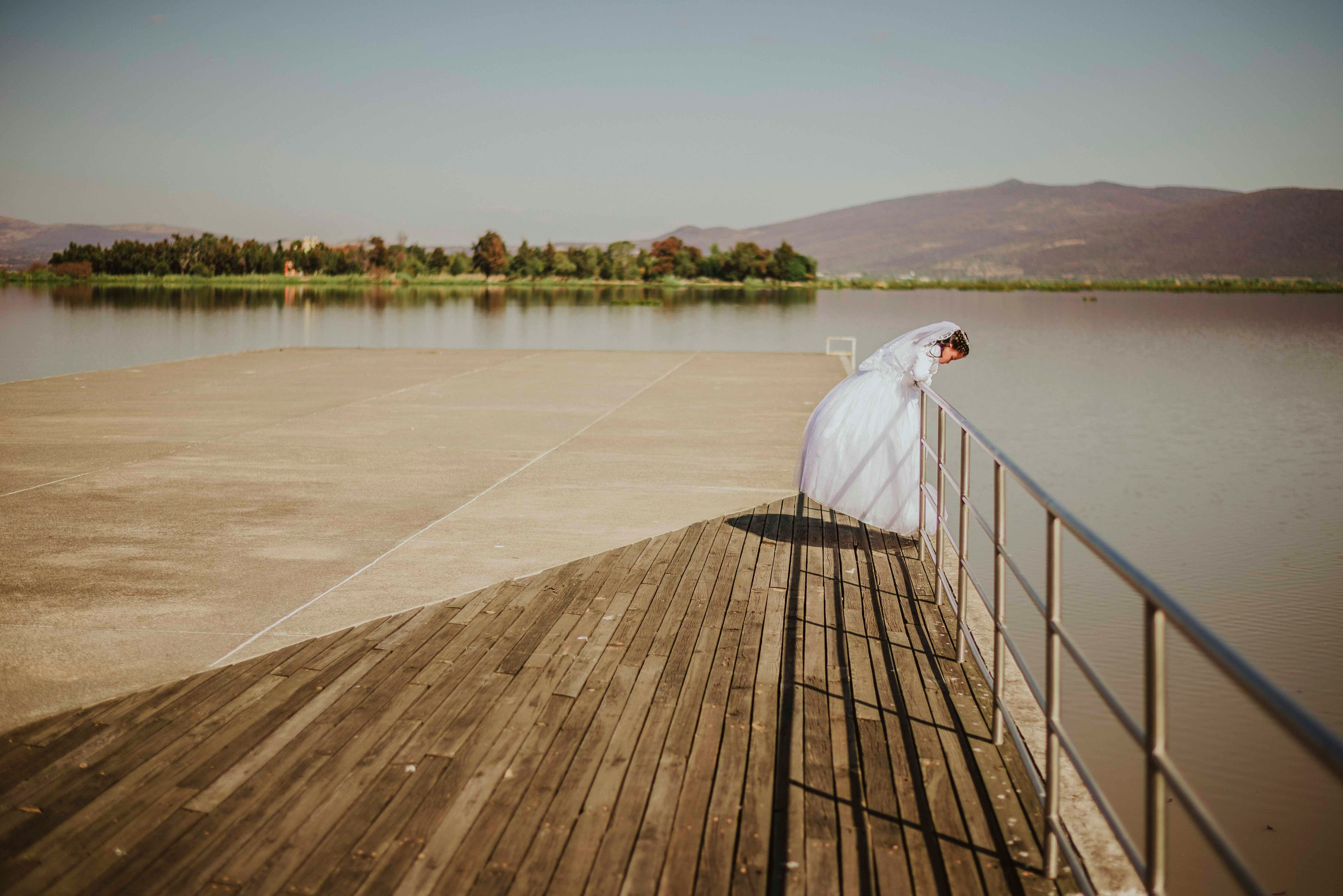 woman wearing wedding dress looking on body of water