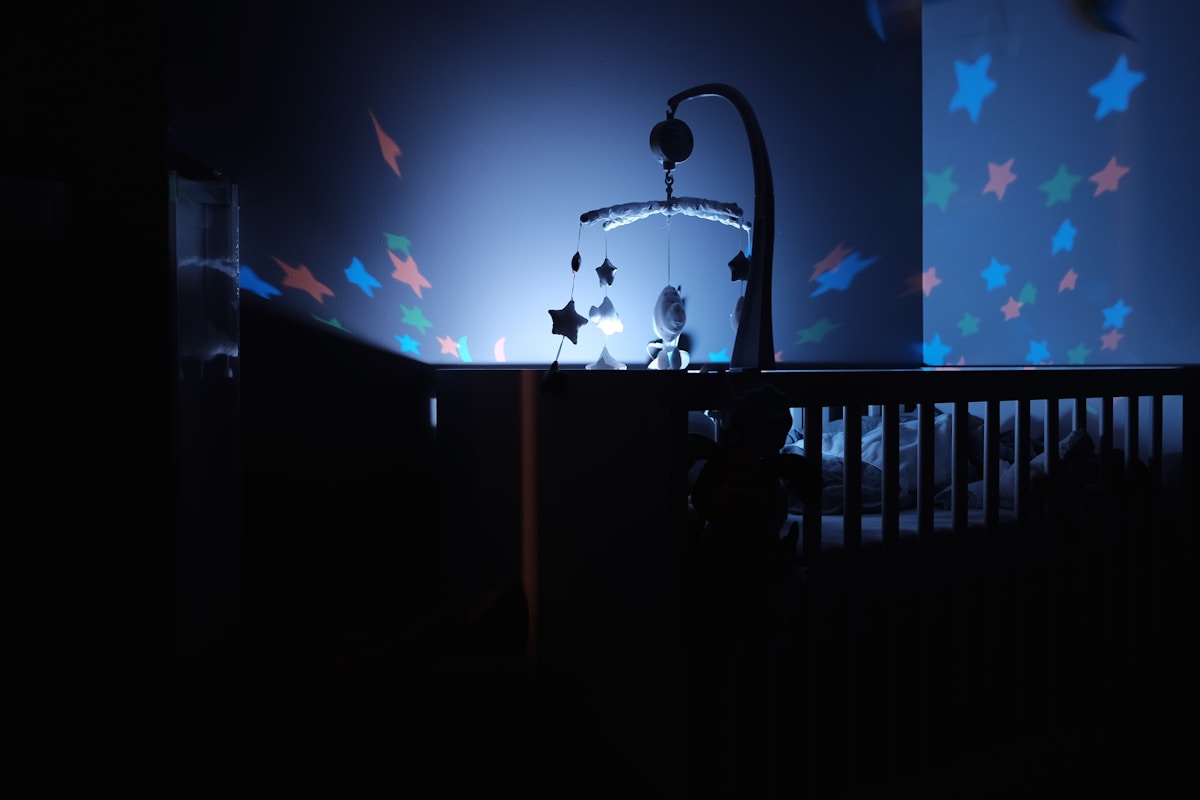 A baby's cot in a darkened room, with stars brojected from a nightlight glowing on the walls.