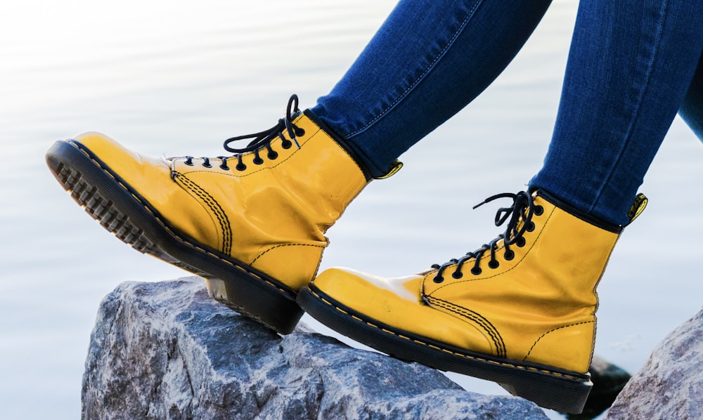 Person mit gelben Doc Martens Airwair-Stiefeln auf grauem Felsen