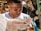 A man intently reads a newspaper titled 'Granma' outdoors, with articles about political events like a visit from Barack Obama. The background is slightly blurred, featuring various objects and people.