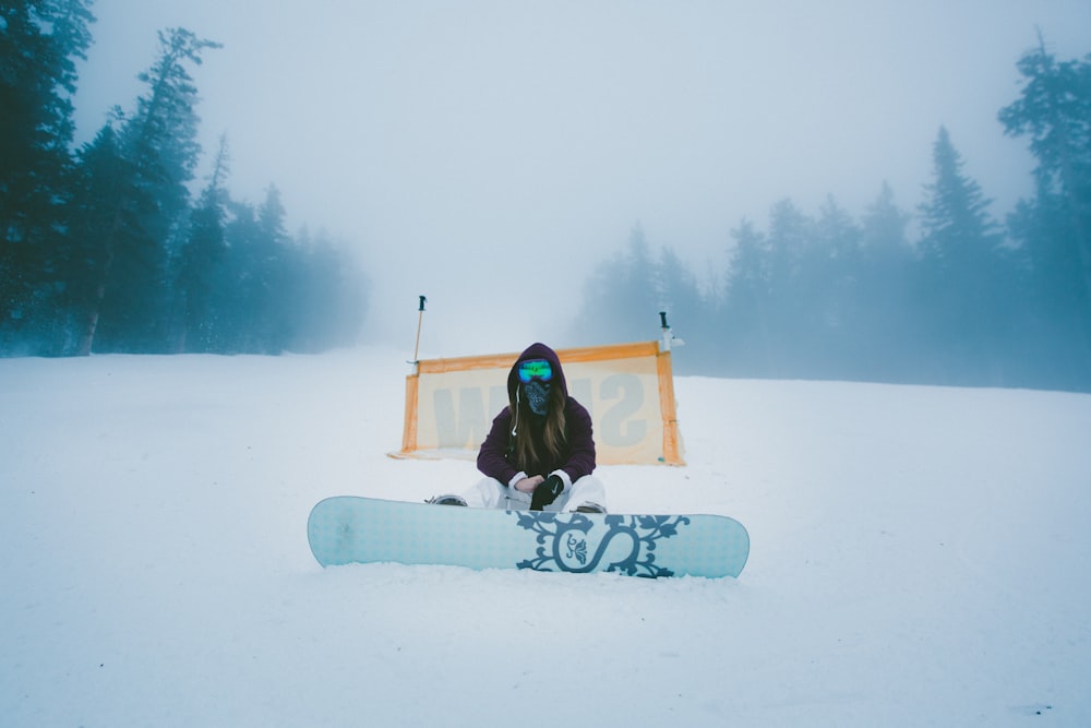 昼間、雪原に座るスノーボードを持つ人