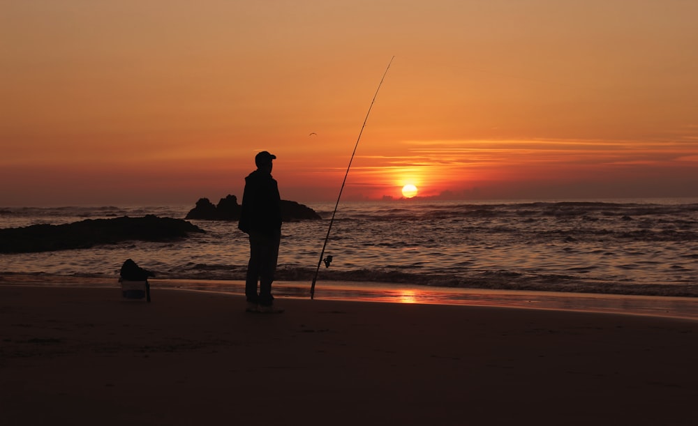 silhouette of man fishing on beach during sunset