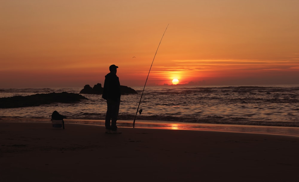 silhueta do homem pescando na praia durante o pôr do sol