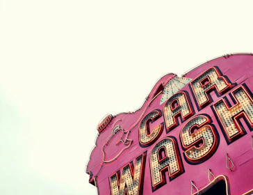 A customer smiling as their car sparkles under retro synthwave neon signs.