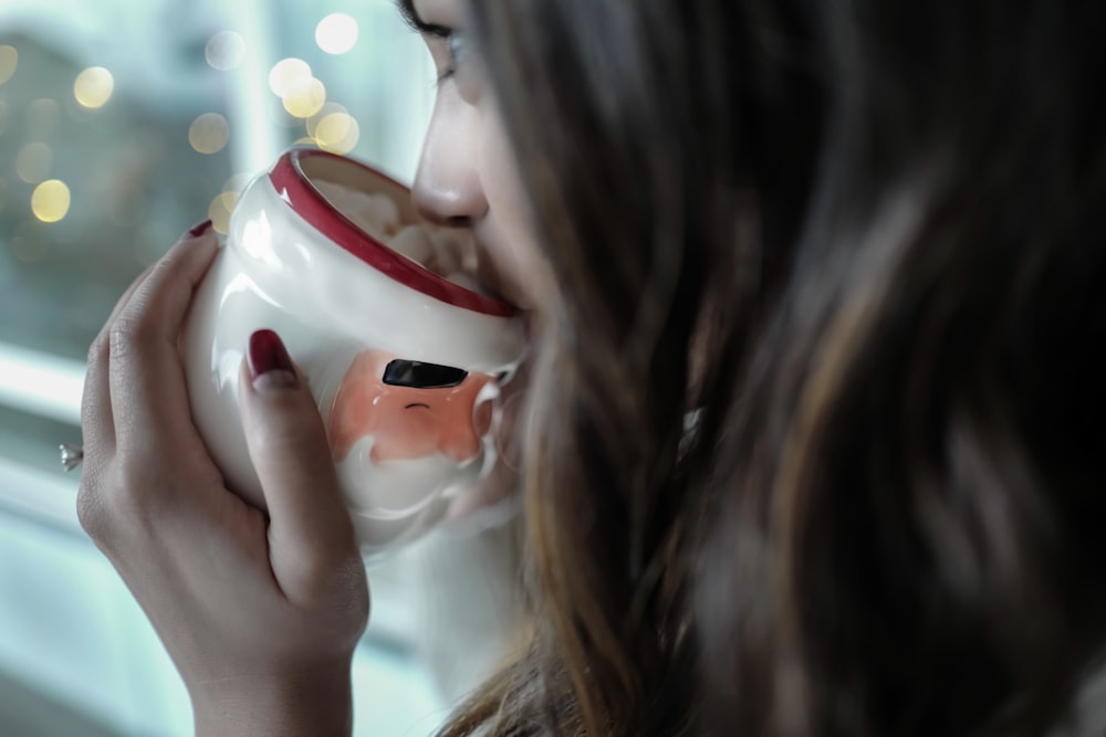 femme buvant sur une tasse en céramique blanche et rouge