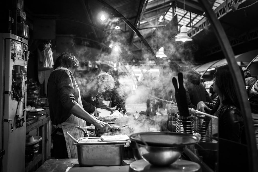 grayscale photography of man cooking beside single-door refrigerator