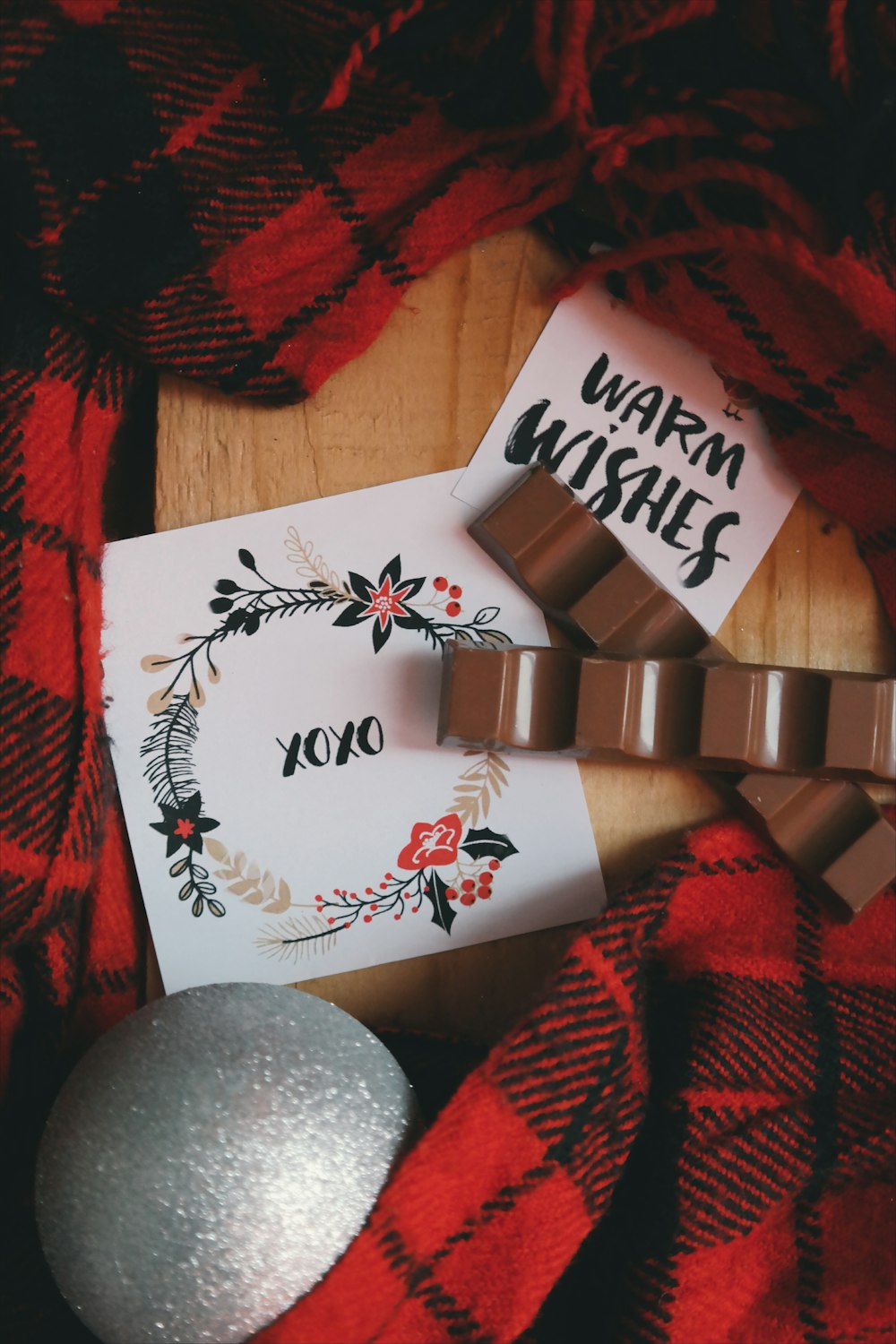An XOXO note next to a gray Christmas ornament and red plaid fabric.