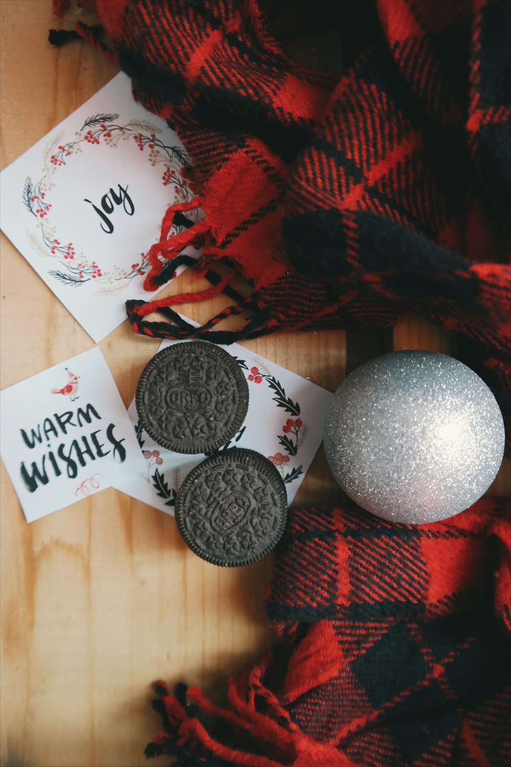 Des biscuits Oreo autour de notes de papier de Noël, d’un ornement et d’un tissu à carreaux rouge.