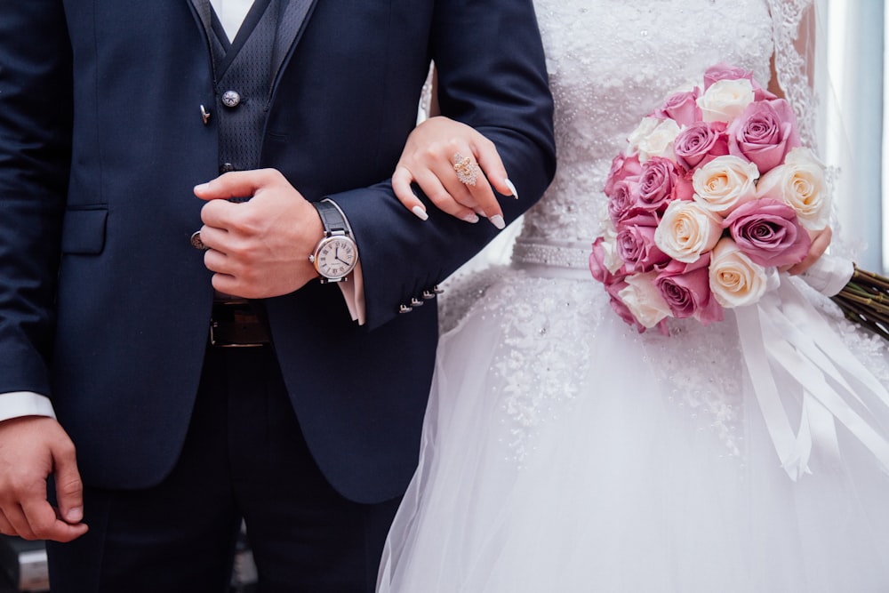 Una novia sosteniendo un ramo de rosas rosas y blancas mientras se abraza con su esposo.