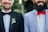 Two smiling men wearing formal attire, one in a black suit with a black bow tie and floral boutonniere, the other in a light blue suit jacket with a white shirt and bright red bow tie. Both have beards and are photographed from the chest up, standing side by side against a blurred green background.