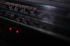 A close-up view of a vintage stereo radio cassette recorder. The focus is on the frequency display, which includes various numbers and units such as 540, 600, and 120m. Two small red indicator lights are glowing beneath the display, hinting at the device being powered on.