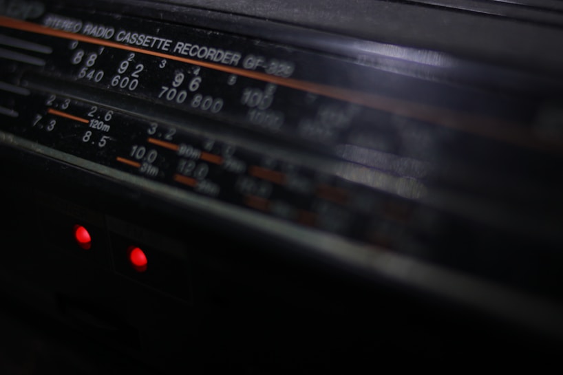 A close-up view of a vintage stereo radio cassette recorder. The focus is on the frequency display, which includes various numbers and units such as 540, 600, and 120m. Two small red indicator lights are glowing beneath the display, hinting at the device being powered on.