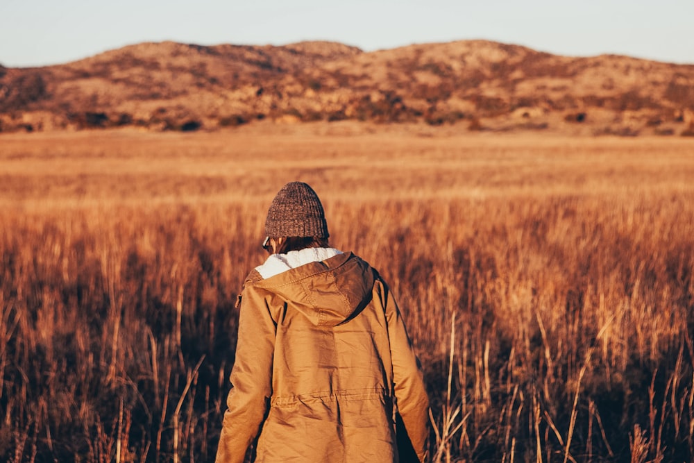 person wearing jacket walking in brown grass field