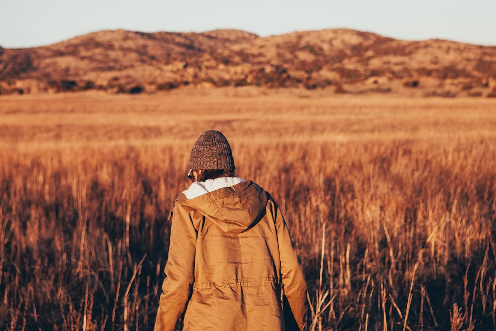 Persona che indossa la giacca che cammina nel campo di erba marrone