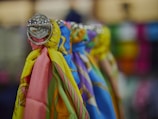 A close-up view of colorful scarves hanging on a rod, showcasing vibrant patterns and a glossy metal fixture. The background appears blurred, highlighting the focus on the fabric textures and hues.
