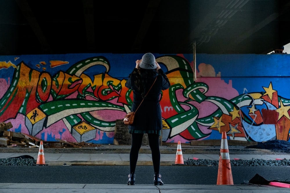 Frau im blauen Mantel steht vor Wandgraffiti