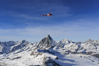 A helicopter soaring above the Himalayan mountain range under a clear blue sky.