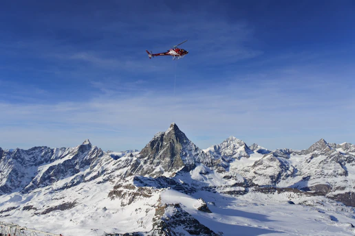 A helicopter soaring above the Himalayan mountain range under a clear blue sky.