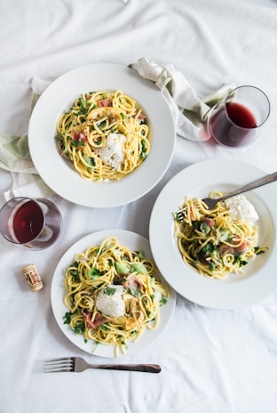 three round white plates with pasta near two glass cuups