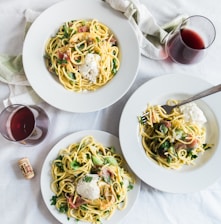 three round white plates with pasta near two glass cuups