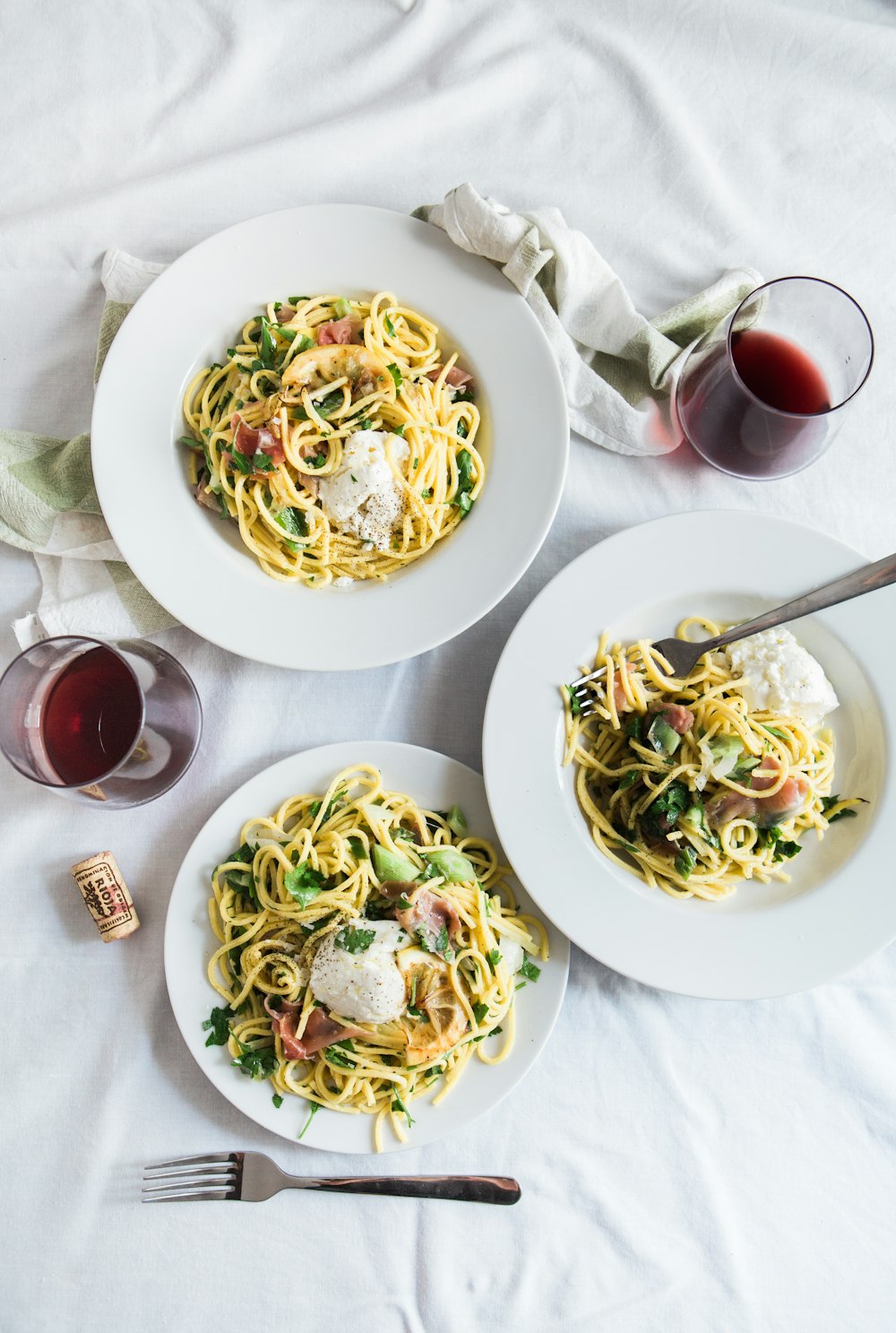 three round white plates with pasta near two glass cuups