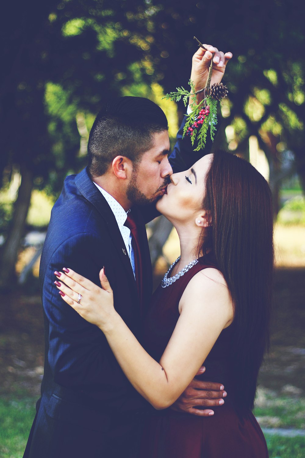 man and woman kissing near trees