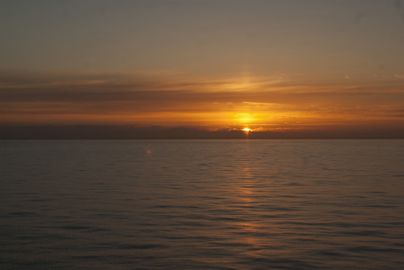 A serene sunrise over a calm ocean, with soft royal blue and silver hues reflecting on the water.