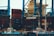 A large shipping port with numerous stacked cargo containers, cranes, and two small boats docked at the harbor. The containers are primarily red and blue and labeled with 'KMTC'. The cranes are towering, painted in blue, with the word 'NORTHPORT' prominently displayed. The scene is industrial, indicating a bustling area for shipping and logistics.