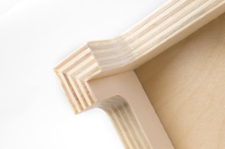 A close-up view of a wooden corner joint, displaying the intricate pattern of layered wood grain and precise craftsmanship. The natural wood color gives it a simple yet elegant appearance.