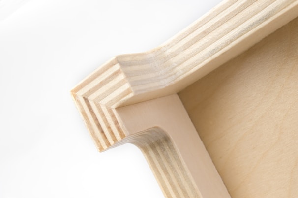 A close-up view of a wooden corner joint, displaying the intricate pattern of layered wood grain and precise craftsmanship. The natural wood color gives it a simple yet elegant appearance.