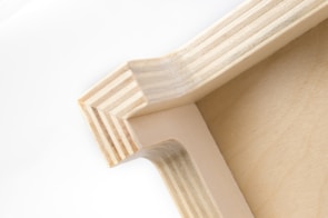 A close-up view of a wooden corner joint, displaying the intricate pattern of layered wood grain and precise craftsmanship. The natural wood color gives it a simple yet elegant appearance.
