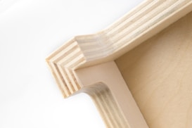 A close-up view of a wooden corner joint, displaying the intricate pattern of layered wood grain and precise craftsmanship. The natural wood color gives it a simple yet elegant appearance.