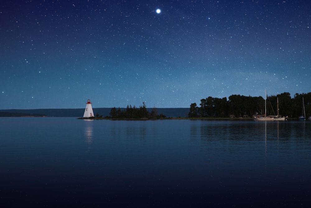 photograph of white lighthouse near calm body of water at night