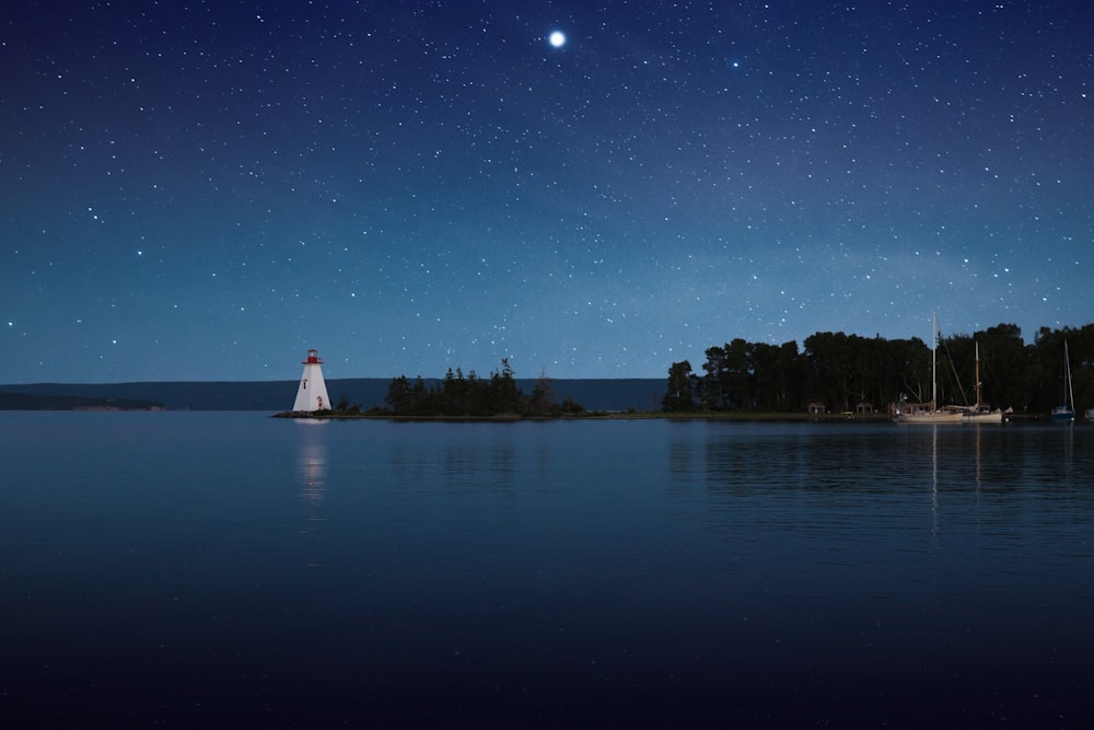 fotografia del faro bianco vicino allo specchio d'acqua calmo di notte